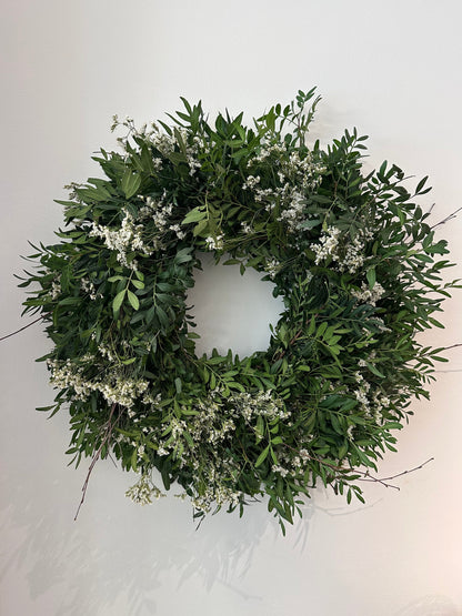 Corona natural con flores blancas y follaje verde, colocada sobre una puerta